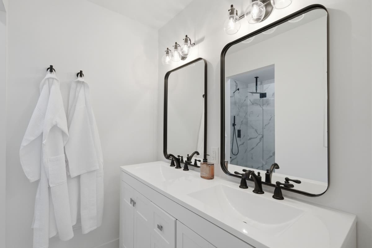 Double vanity with black-framed mirrors, black faucets and robes on hooks.