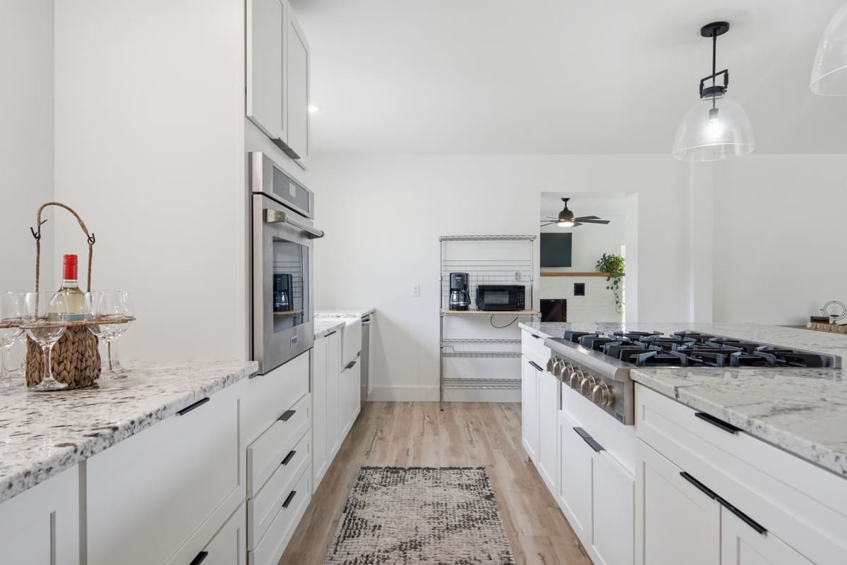 Galley view of the kitchen with a gas range, stone counters and pendant lights.