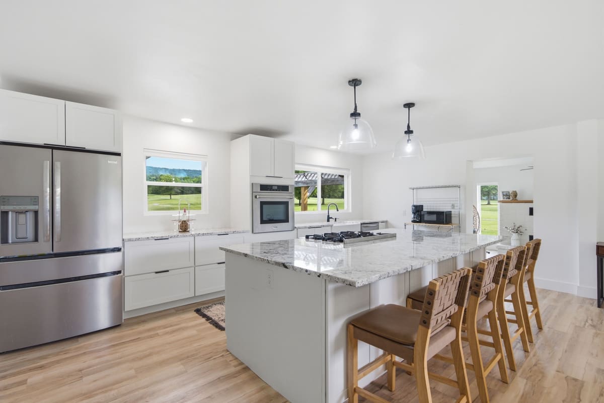 White shaker kitchen with a stone-topped island, leather counter stools and pro-grade appliances.