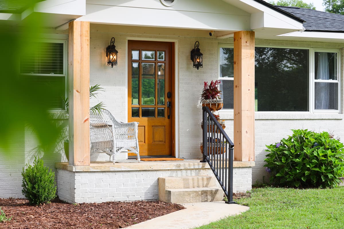 Covered front porch with cedar posts, black iron lanterns and a wood-and-glass front door.