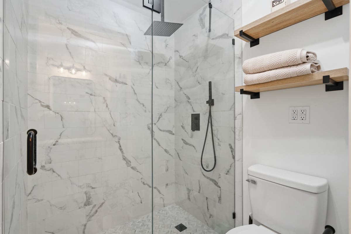 Walk-in shower with marble tile, a rain head and black fixtures behind a glass door.